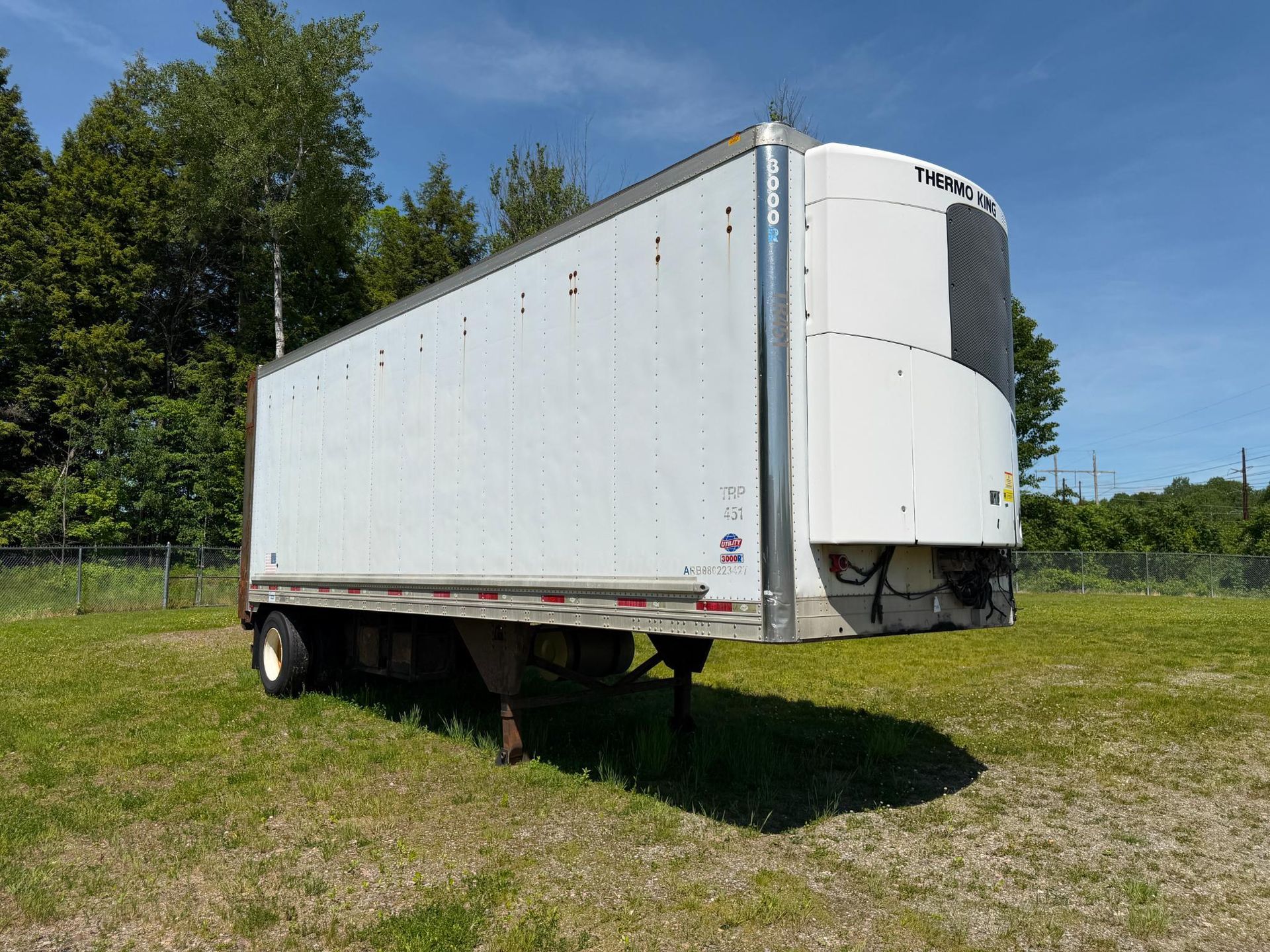 White box trailer parked on grass under a blue sky, with trees in the background