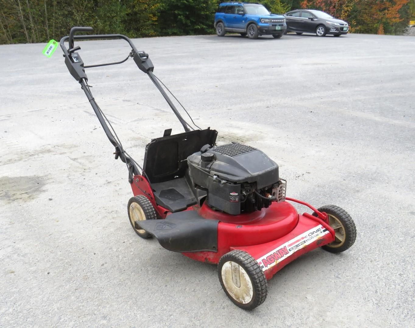 Red lawnmower on a paved surface, handle up, small engine.