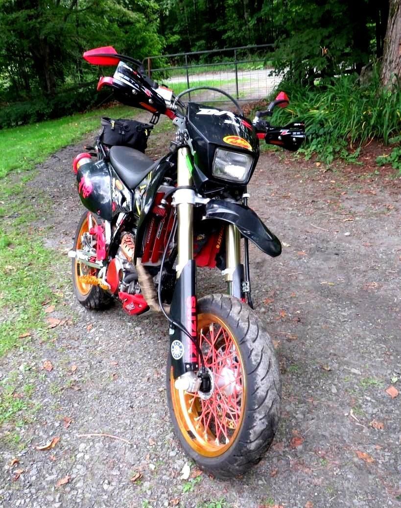 Black and red motorcycle with gold rims parked on a gravel path near trees.