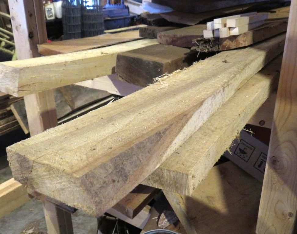 Wooden planks of varying sizes are stacked on a wooden shelf in a cluttered workshop setting.