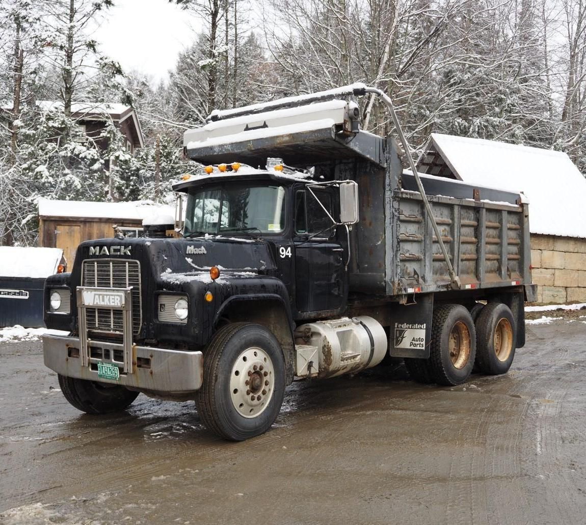 Black Mack dump truck on a snowy day, parked in front of buildings.