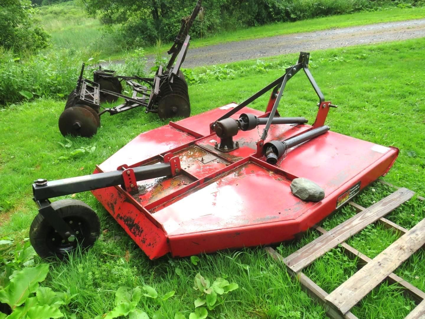 Red rotary mower on green grass.