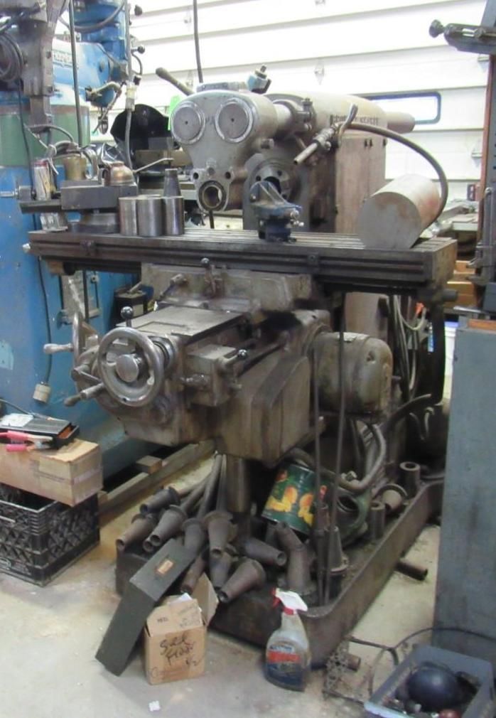Large, industrial milling machine with a gray body, covered in tools, in a workshop setting.