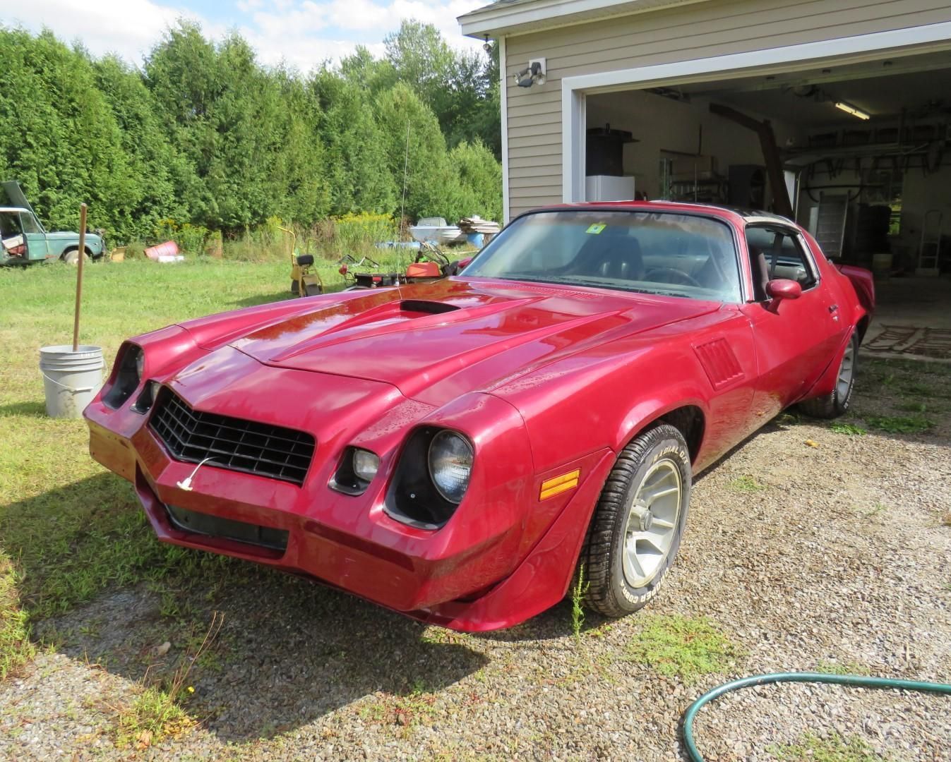 Red 1978 Chevrolet Camaro parked in a yard with a garage in the background.