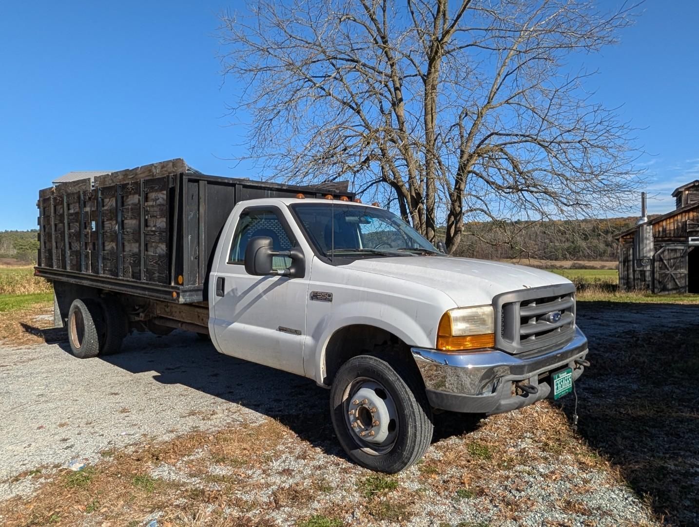 White dump truck parked on a gravel driveway beside a leafless tree and house under a blue sky