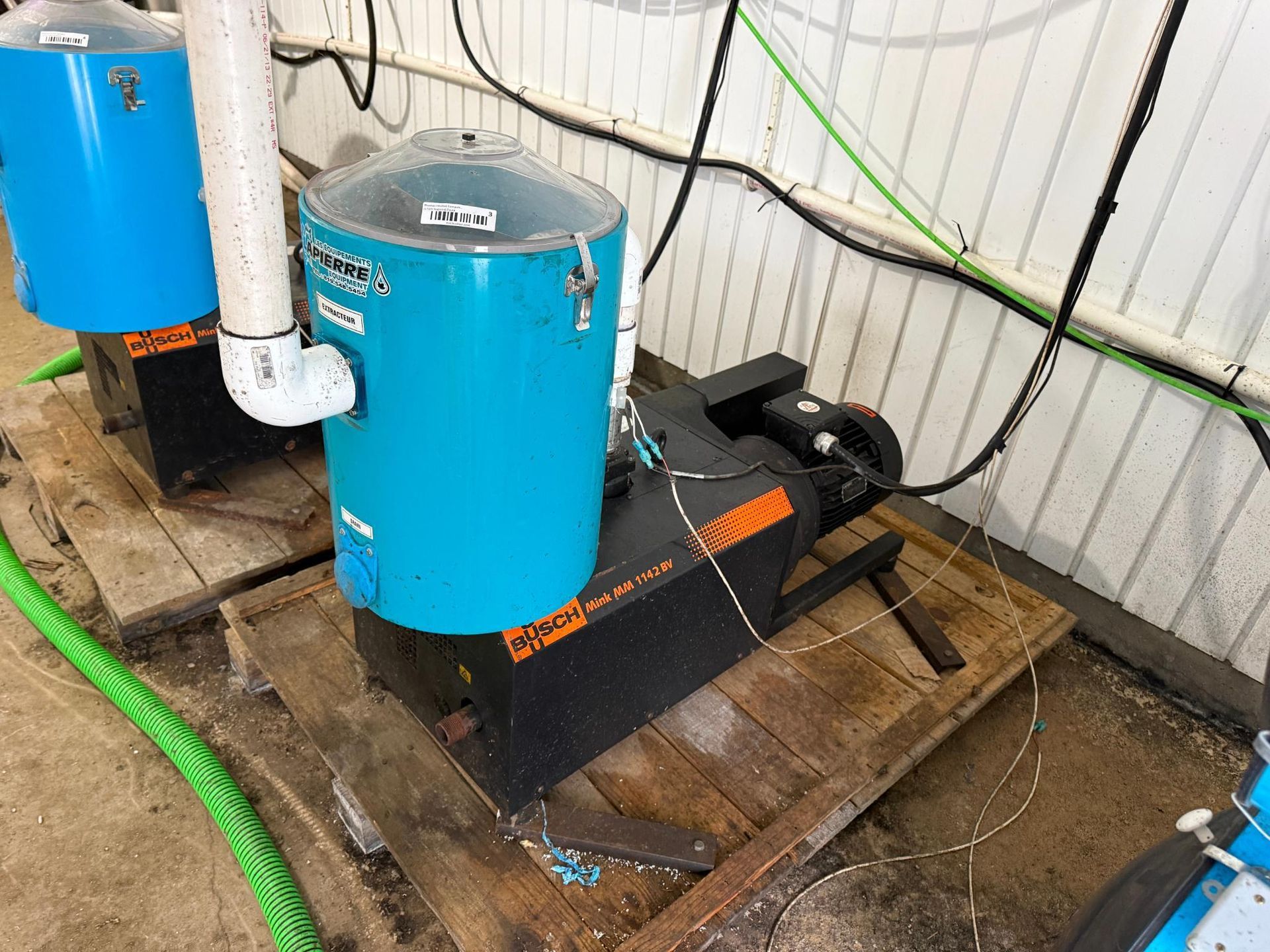 Two blue tanks and a black machine on a wooden pallet, pipes, and electrical cords in a room.