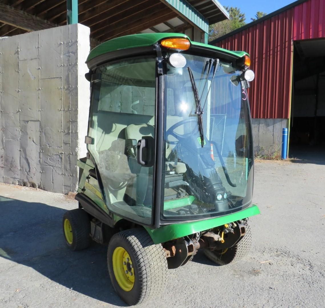 Green John Deere utility vehicle with a glass enclosed cab, parked outside.