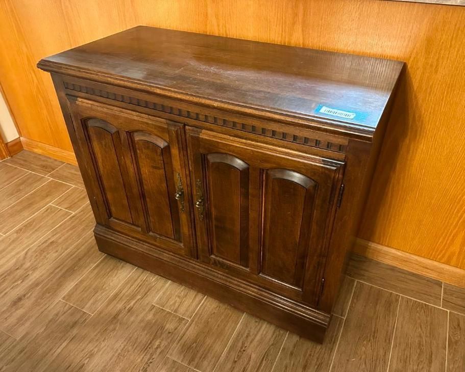 Brown wooden cabinet with two doors, on a wood floor, near a wood-paneled wall.