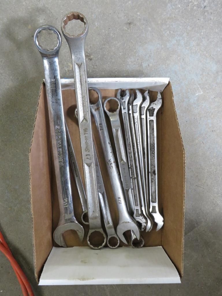Wrenches in a cardboard box, varying sizes, gray metal, arranged on a light surface.