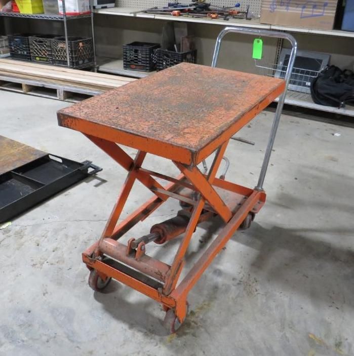 Orange scissor lift cart with handle and wheels, on a concrete floor.