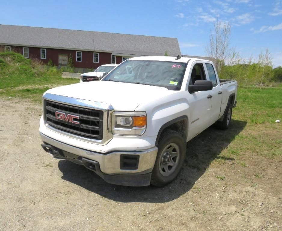 White GMC pickup truck parked in front of a red building on a sunny day.