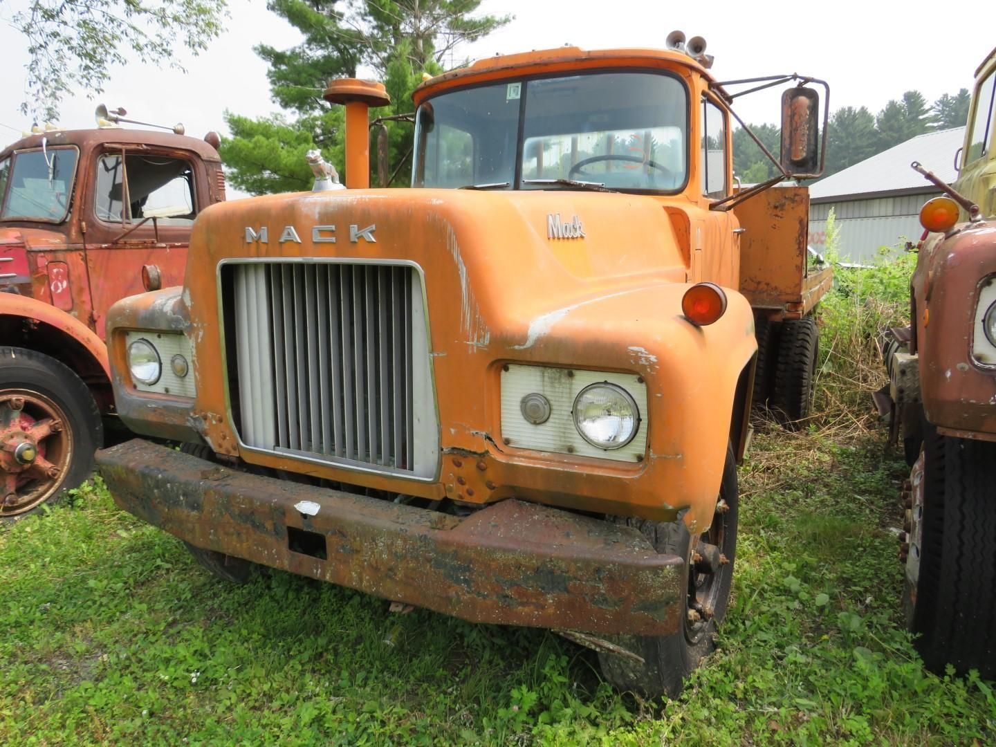 Orange Mack truck with grill and bumper, parked on grass.