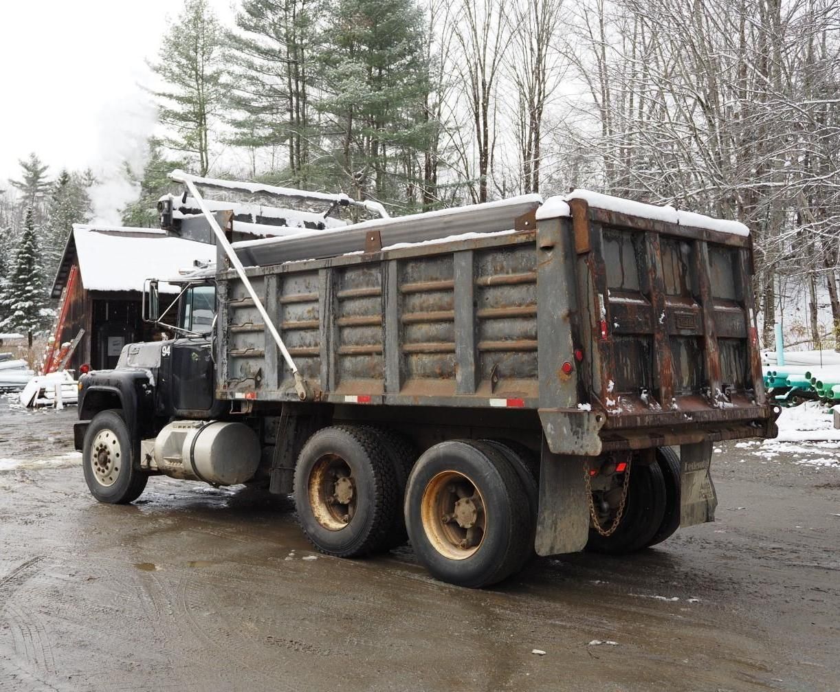 Black dump truck with a bed, parked on a snowy road, trees in the background.