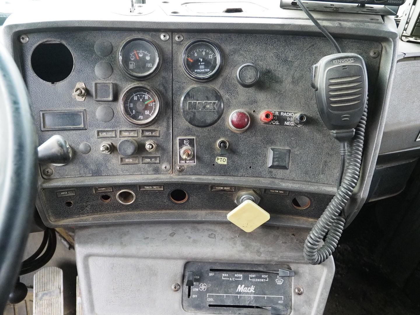 Dashboard of a Mack truck with gauges, switches, and a CB radio microphone. Gray and black.
