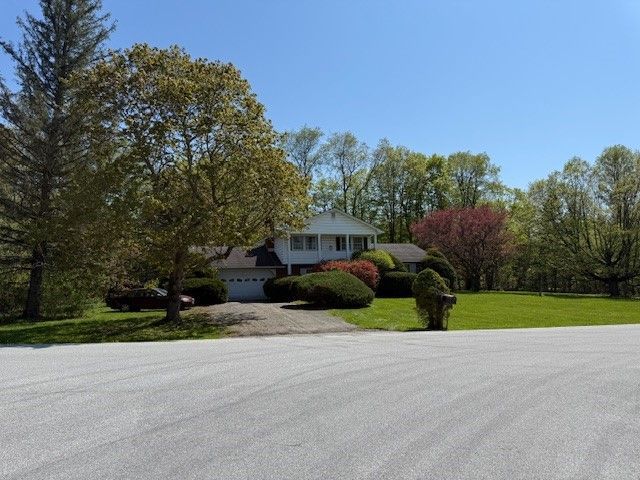 A two-story white house with a garage, surrounded by trees and a green lawn. Blue sky above.