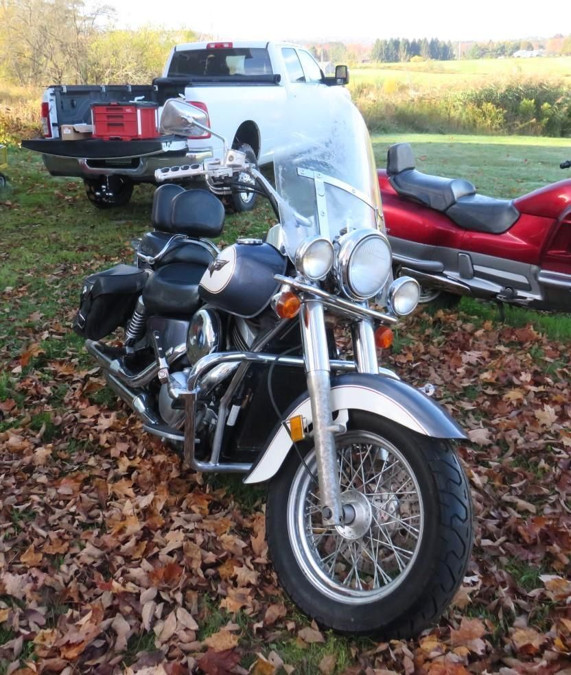 Black motorcycle with chrome details parked on leaves in front of a white truck and red motorcycle.