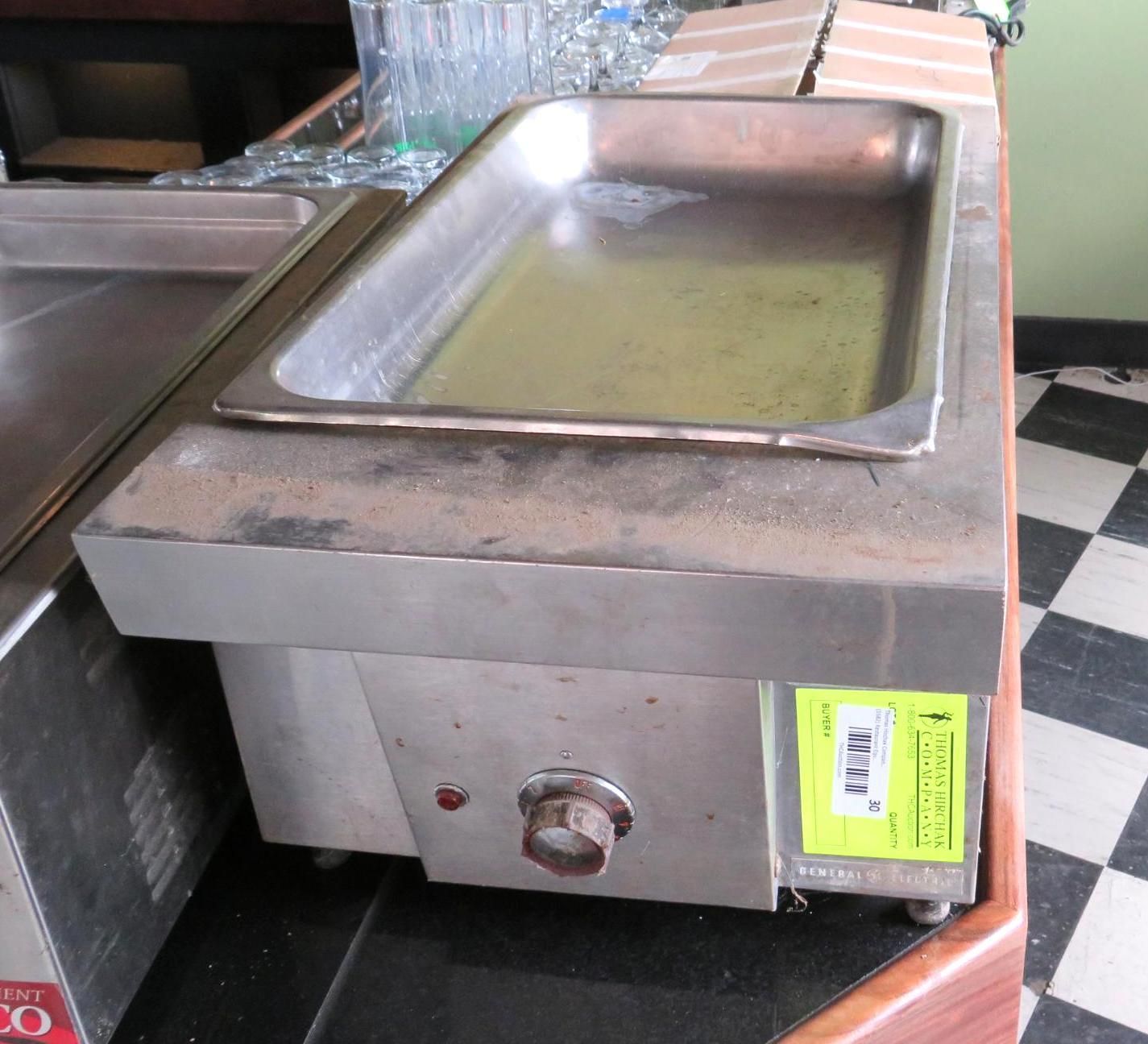 Stainless steel food warmer on a bar with black and white checkered floor.