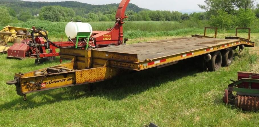 A yellow flatbed trailer with a tractor implement attached, parked in a grassy field.
