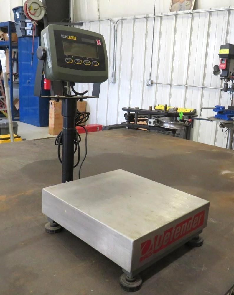 A Defender digital scale on a metal table, in a workshop. The scale is black, gray, and red.