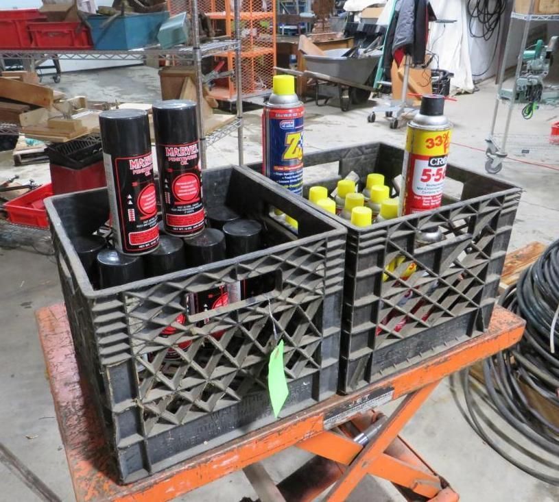 Two black crates on an orange lift, holding cans of spray paint and lubricant.