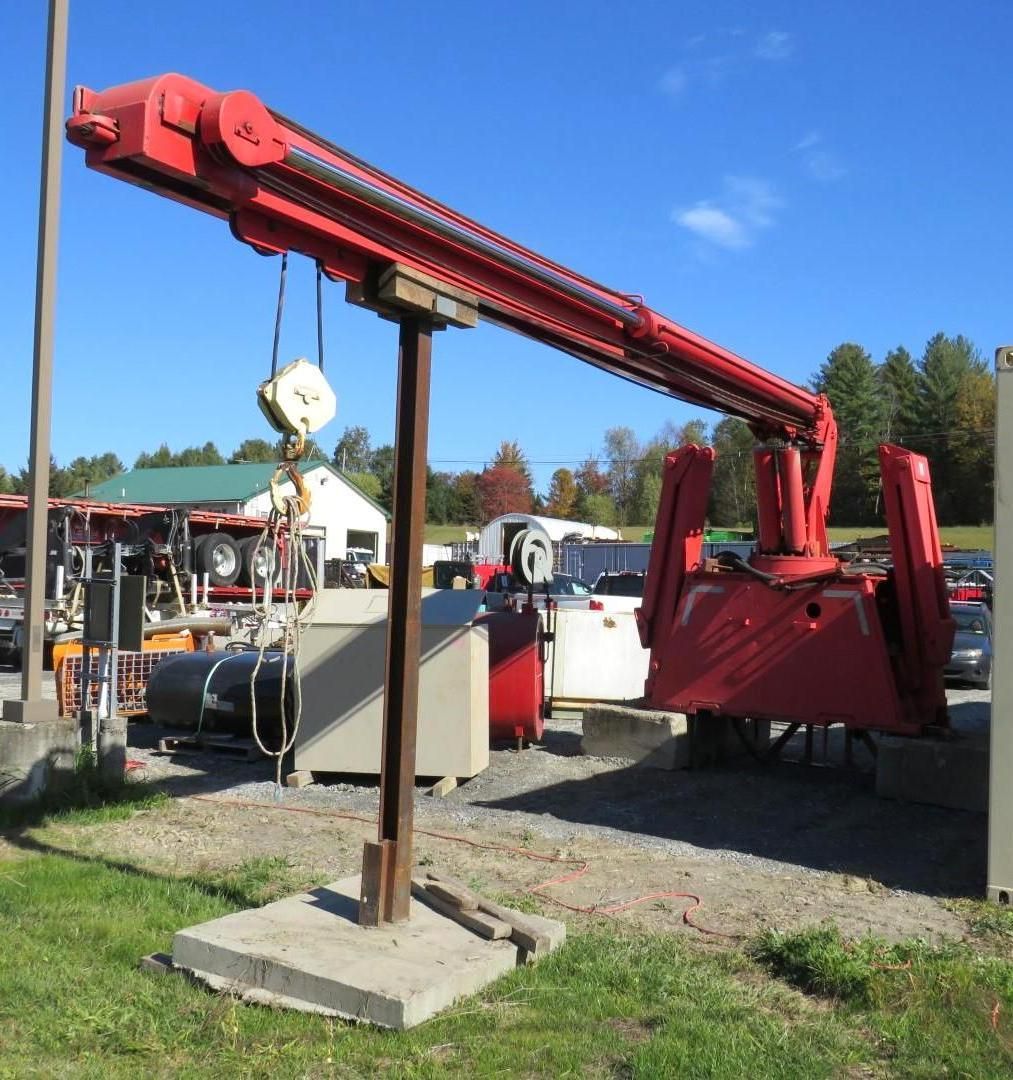 Red industrial crane on a concrete base, outdoors with trees and other machinery in the background.
