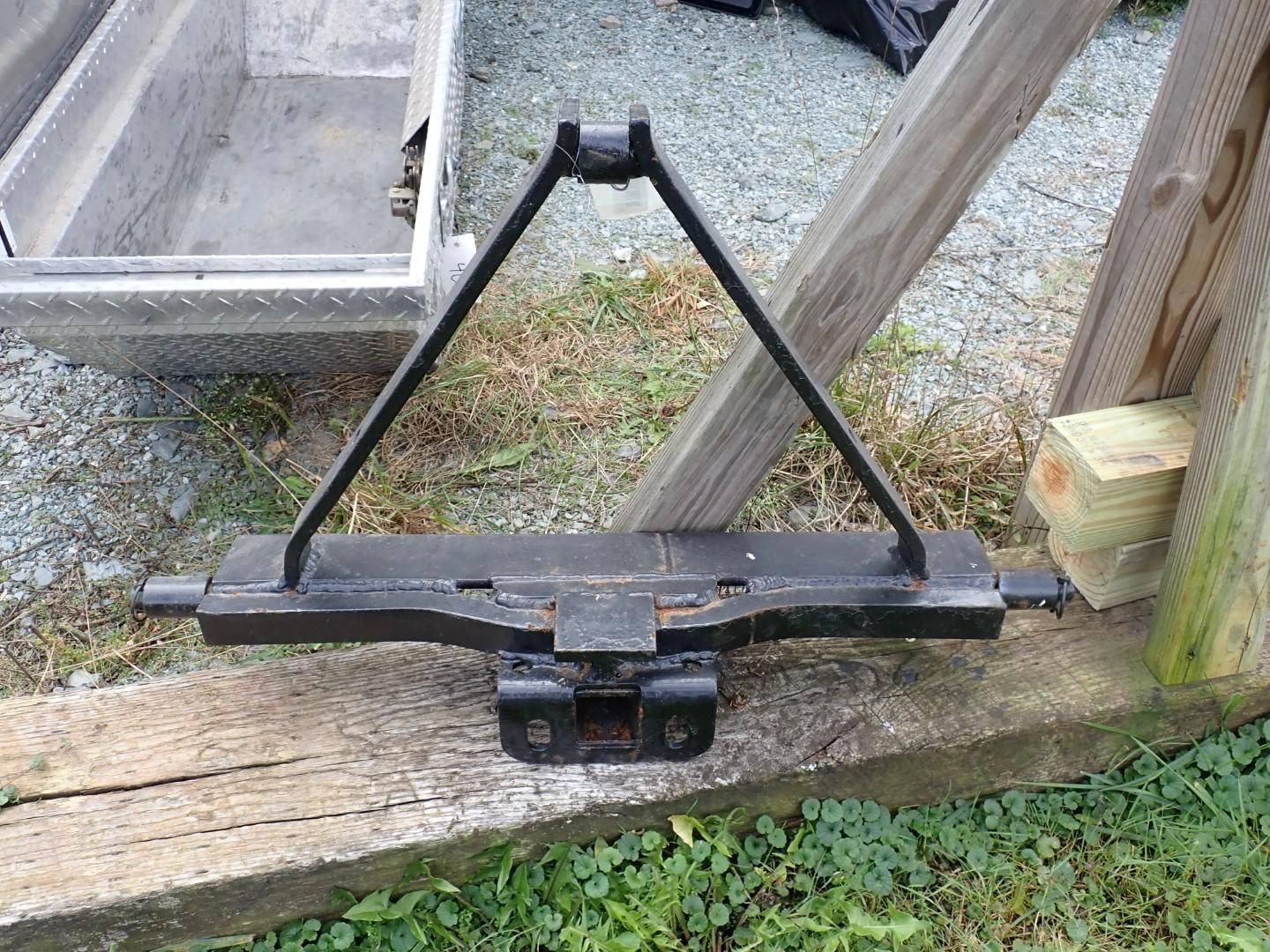 Black metal triangular equipment mounted on a wooden fence outdoors.