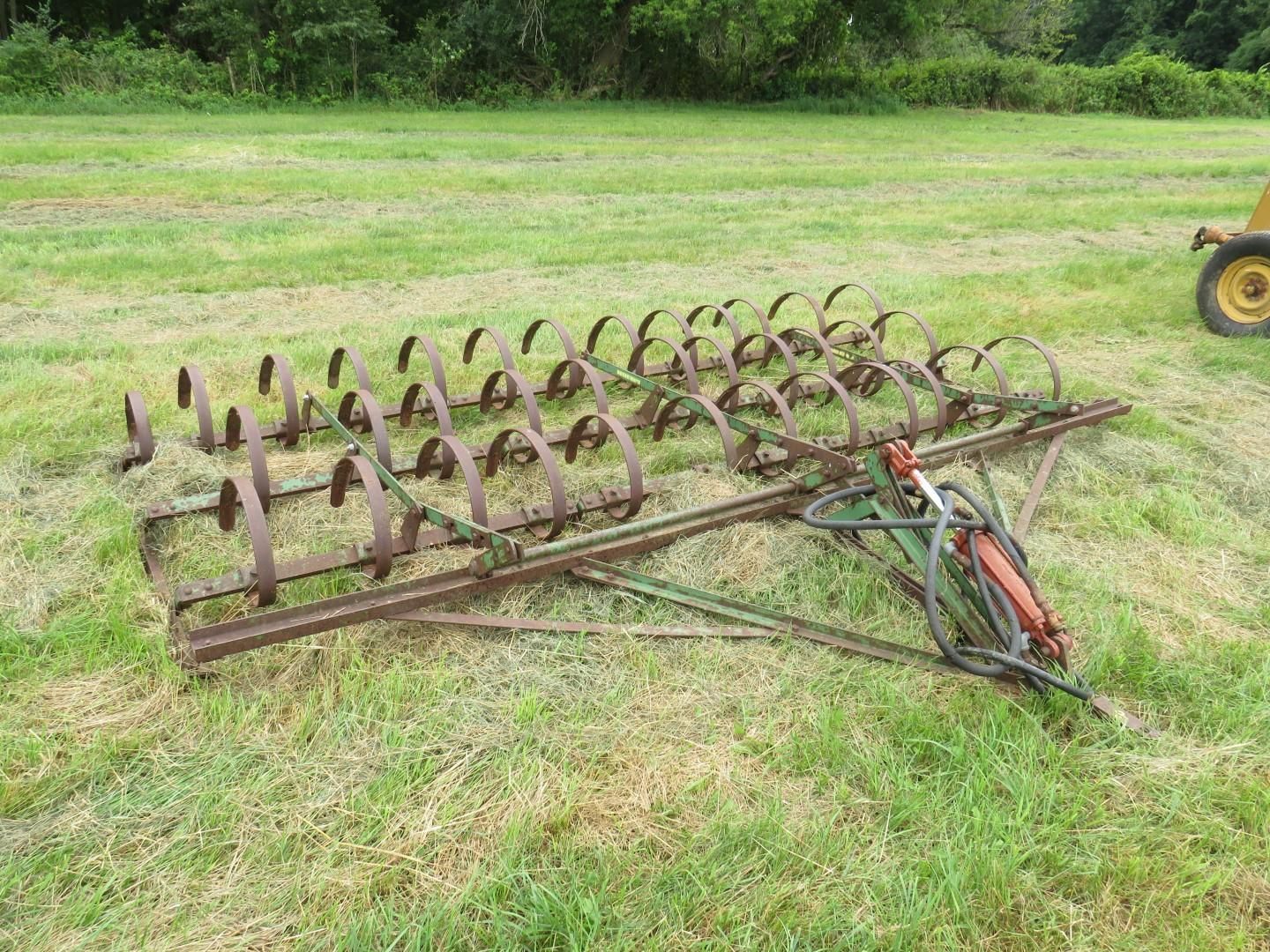 Field harrow with curved tines on a grassy field.