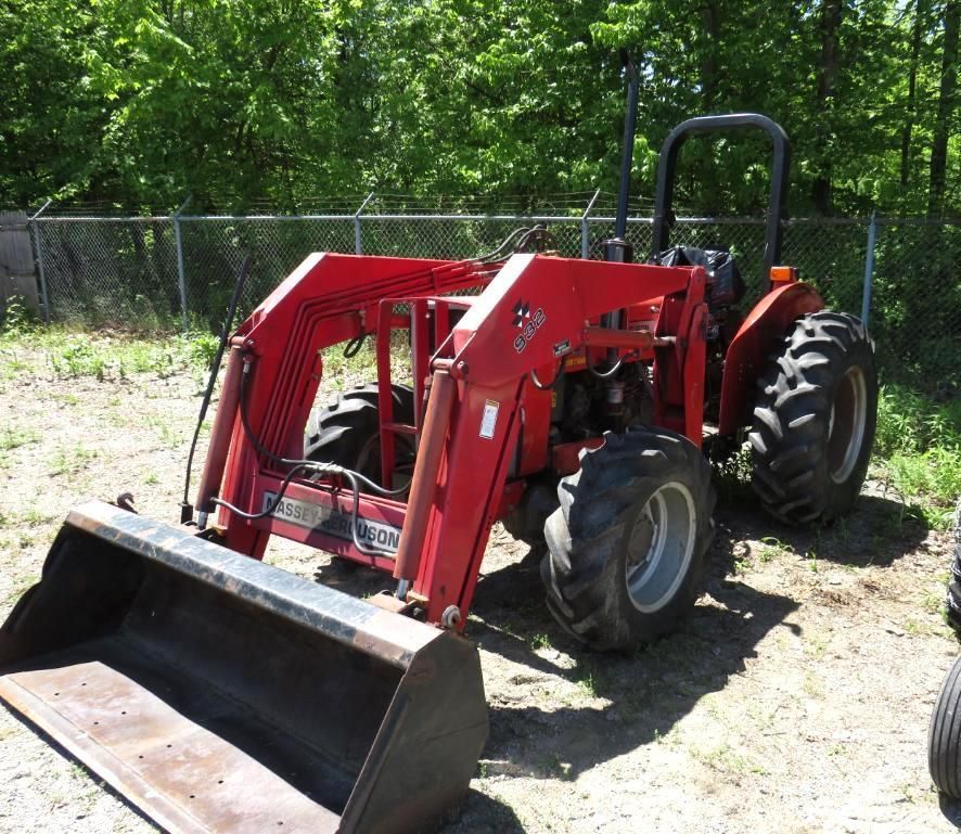 Red tractor with front-end loader and bucket parked outdoors near a fence and trees.