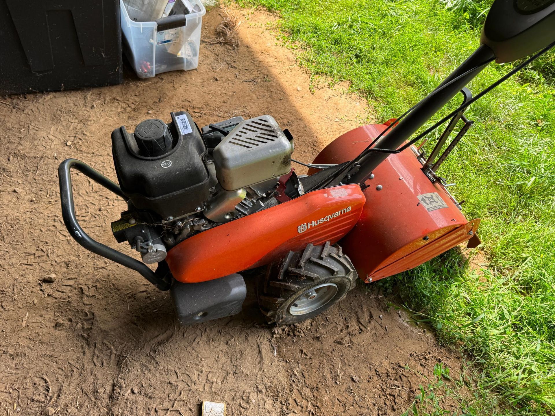 Orange Husqvarna snow blower on dirt and grass.
