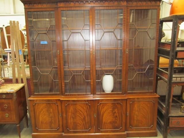 A large, wooden bookcase with glass doors and geometric grilles. It has a base with cabinet doors.