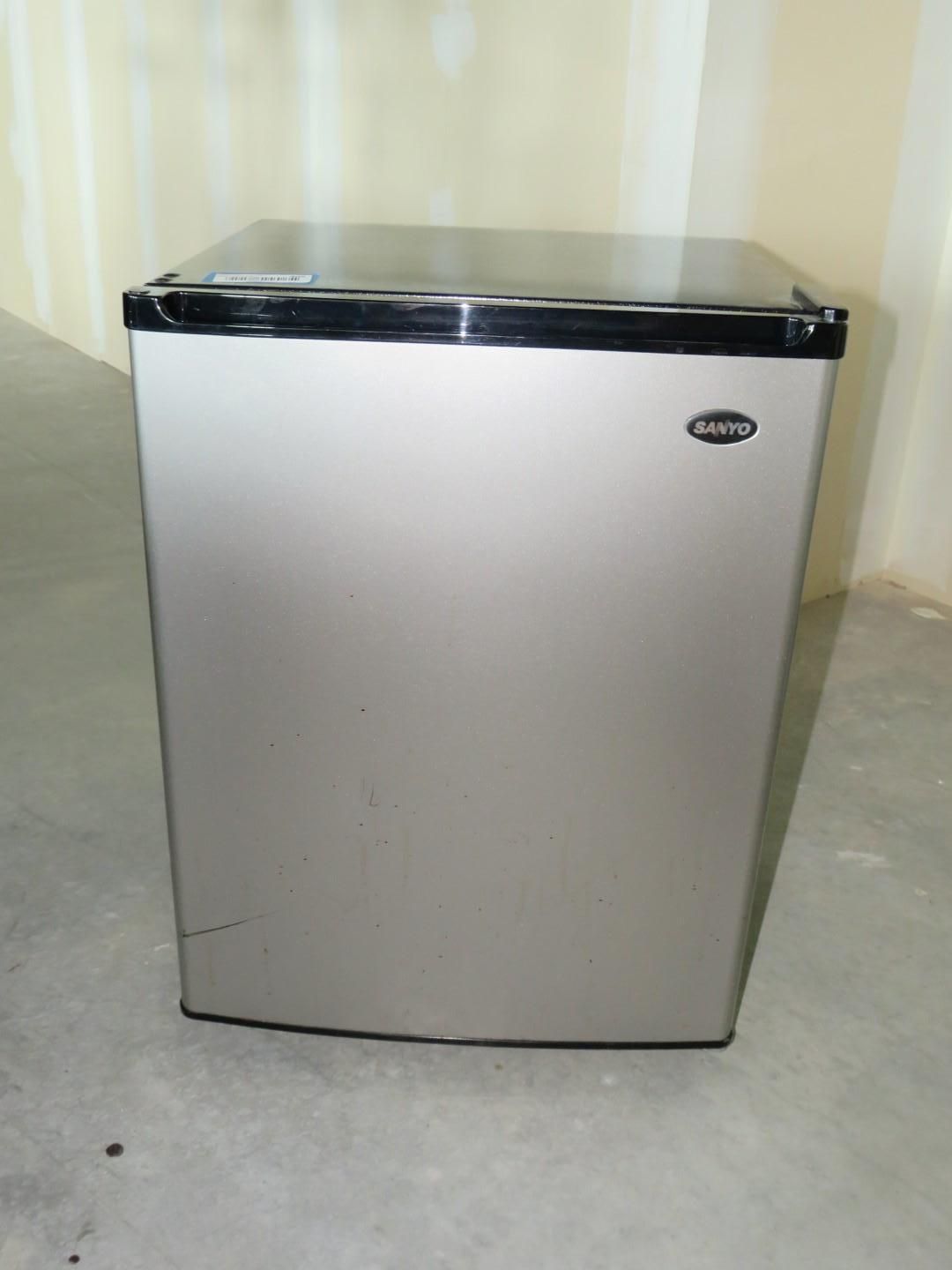 Silver mini-refrigerator on a concrete floor, with black trim and a dark top, against a beige wall.