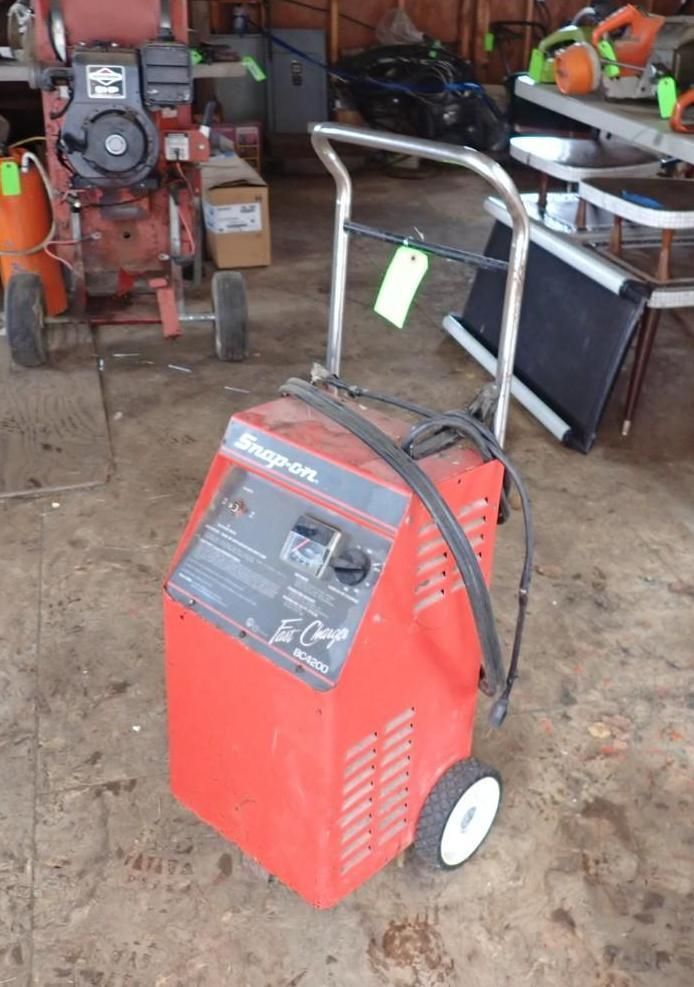 A red Snap-on wheeled battery charger stands in a garage workshop setting.