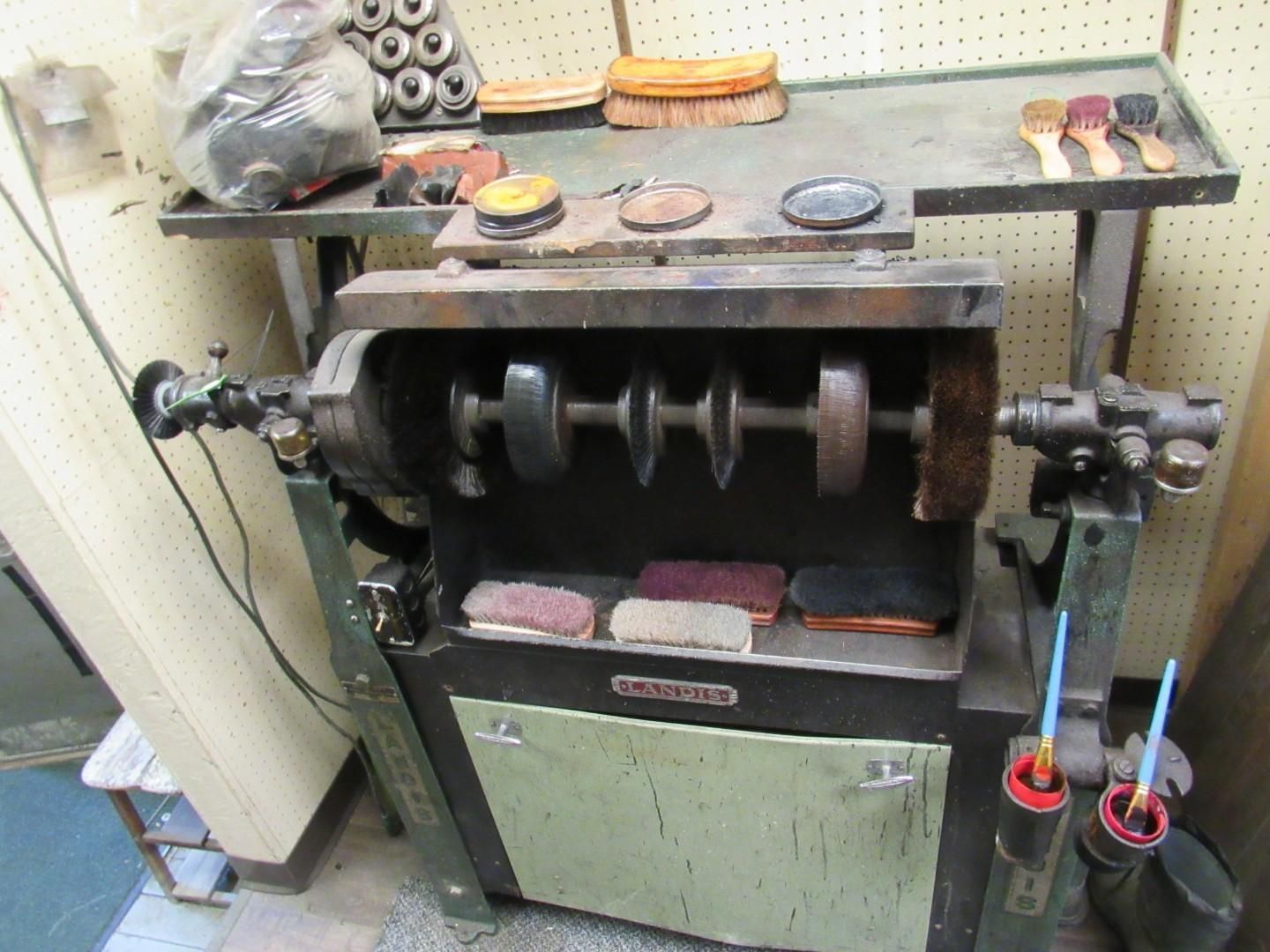 Shoe polishing machine with multiple brushes and buffing pads, workbench in the background.