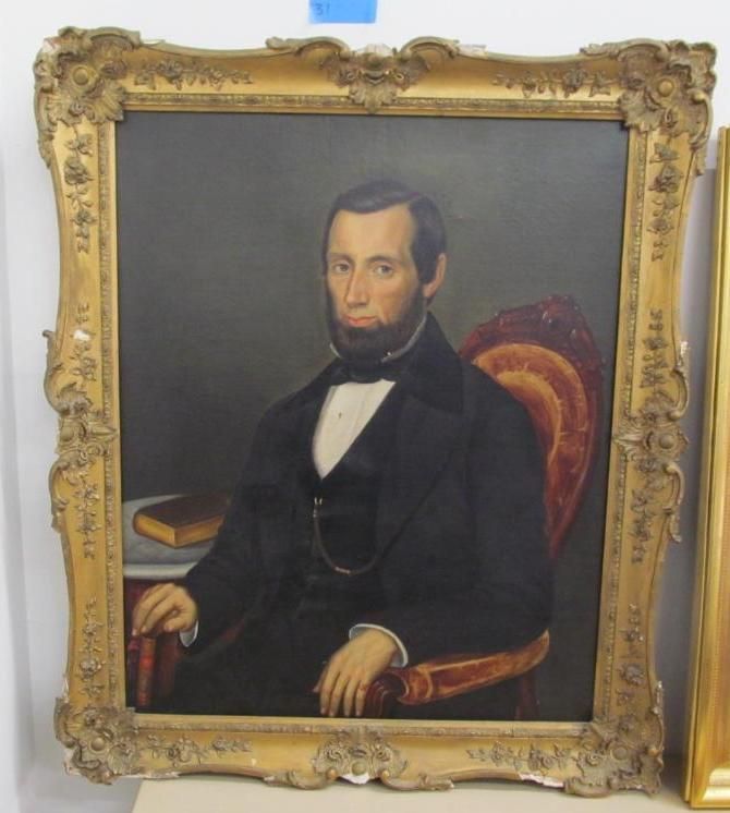 Man's portrait in gold ornate frame; he sits with a book, wearing a dark suit and bow tie.