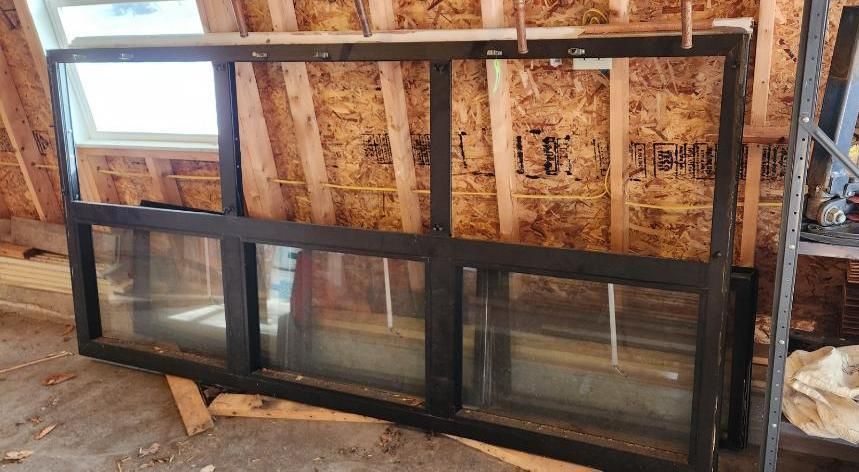 Black-framed window with three panes and a smaller pane, leaning against a wood-paneled wall.