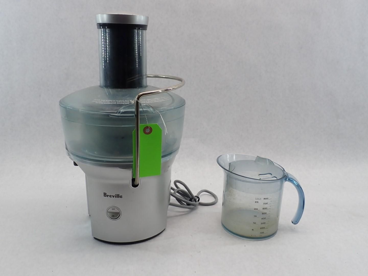 A silver Breville juicer with a green tag next to a measuring cup filled with liquid.