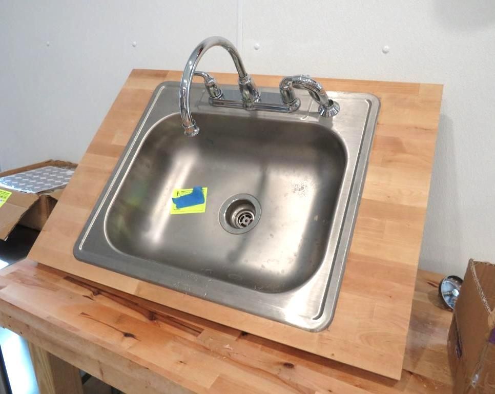 Stainless steel sink installed in a wooden countertop, with chrome faucet against a white wall.
