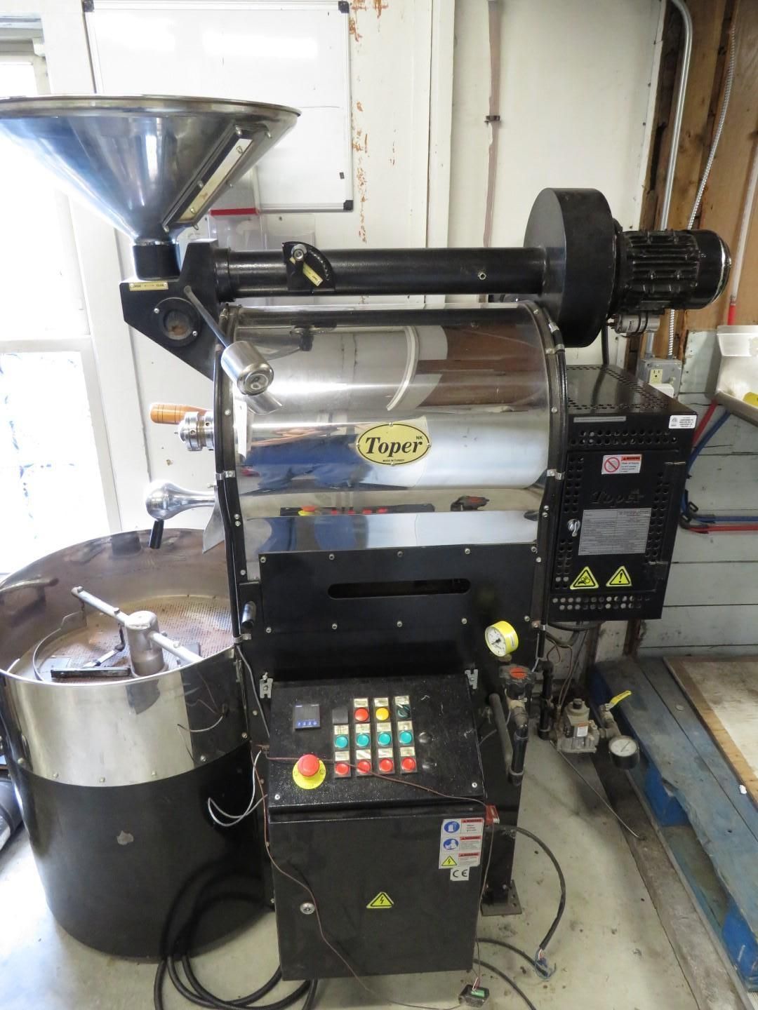 Coffee roaster, silver and black, with hopper, drum, and control panel. Inside a workshop.