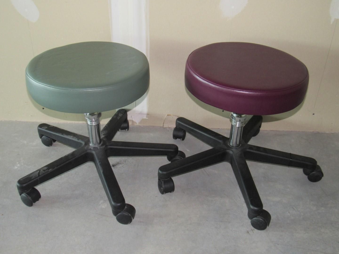 Two adjustable rolling stools: one green, one maroon, on a concrete floor.