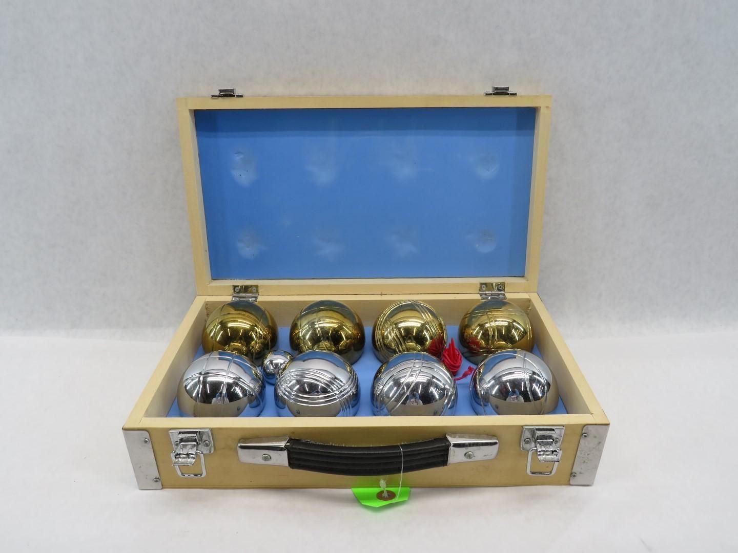Open wooden case with eight metal bocce balls, four gold, four silver, on blue lining.