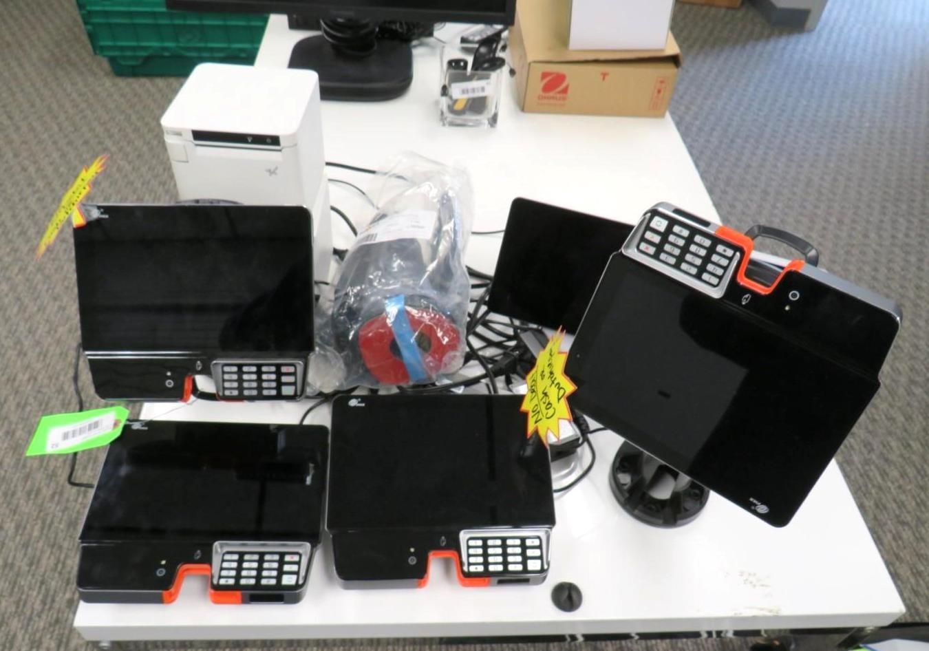 Office desk with multiple black point-of-sale terminals, computer monitors, and other equipment.
