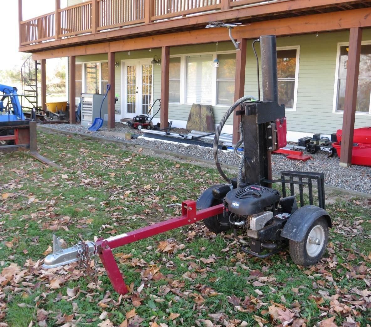Log splitter on wheels, red and black, in a grassy yard near a house.
