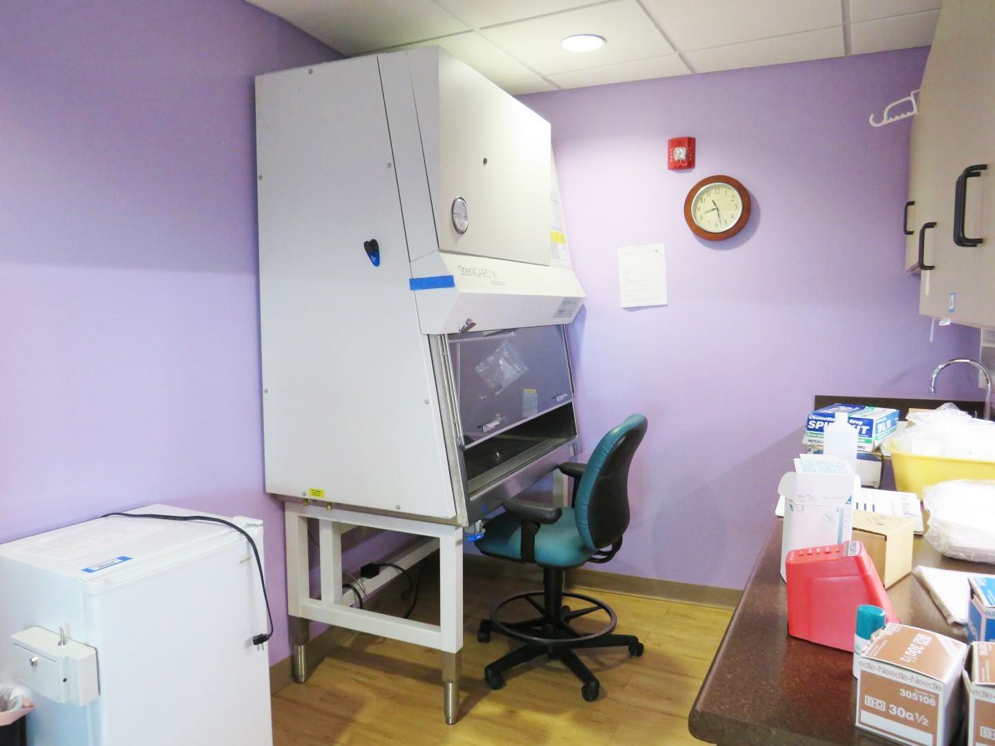 Laboratory room with white biosafety cabinet, chair, and equipment on countertop.