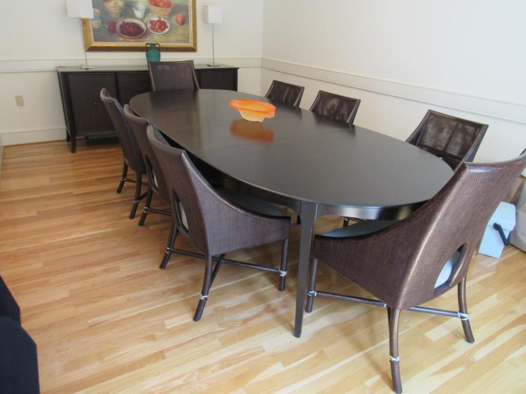 Oval dining table with woven brown chairs in a well-lit room.