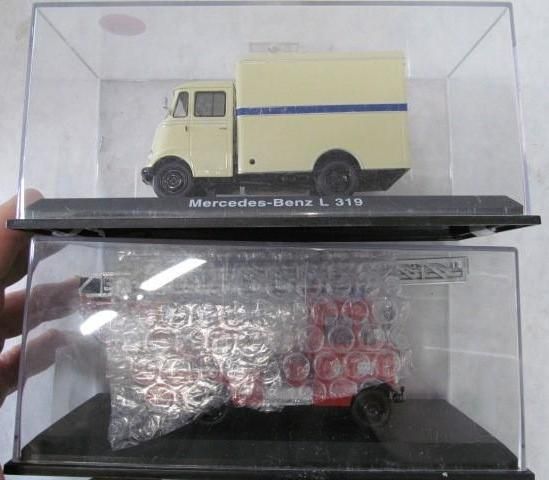 Two model trucks in clear display cases, one tan and blue, the other red and white wrapped in bubble wrap.