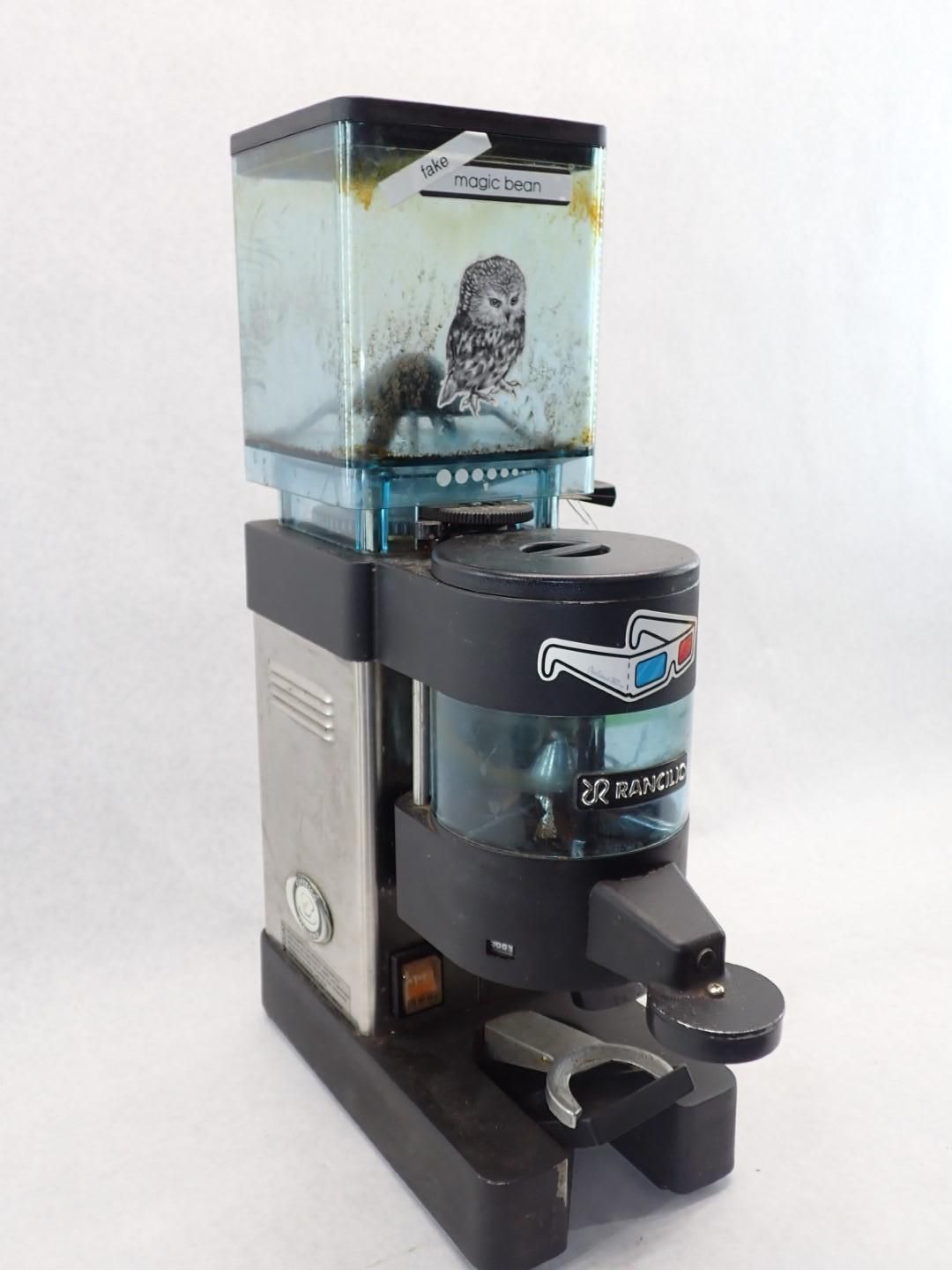 Coffee grinder with a clear hopper, an owl image inside, and a spout for dispensing coffee grounds.