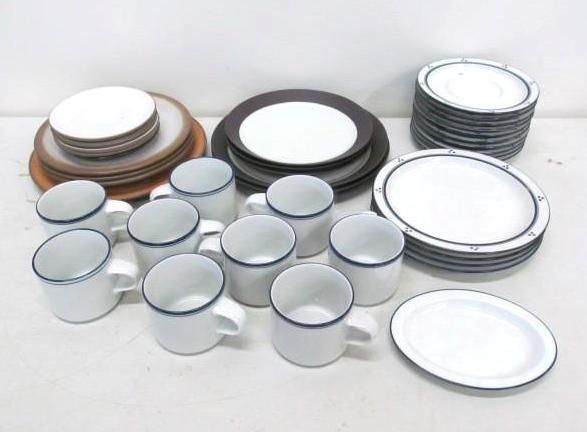 Assortment of white ceramic dishes and mugs with blue trim; includes plates of varying sizes and stacks.