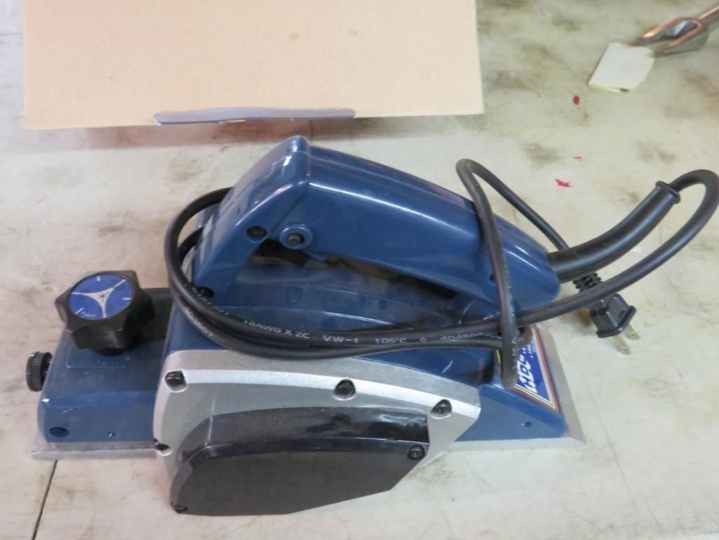 Blue and silver electric hand planer tool with a black cord on a light-colored surface.
