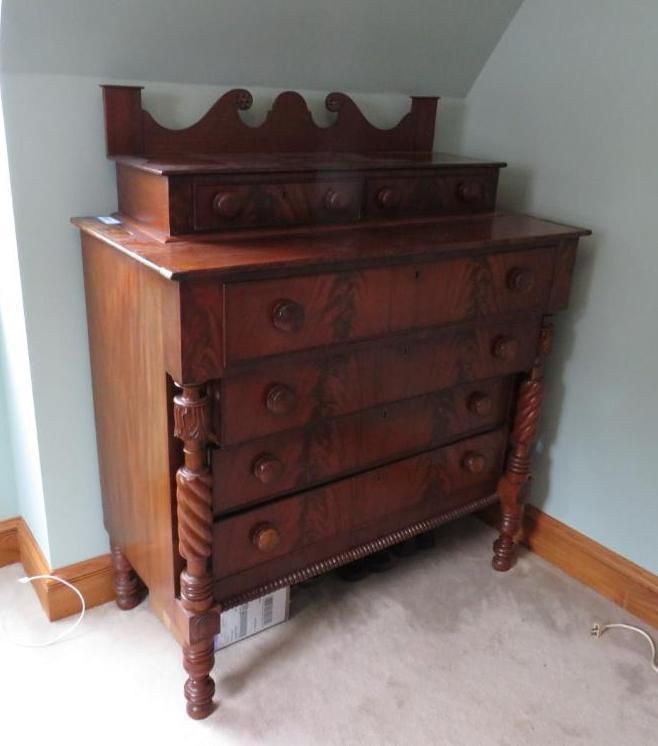 Wooden antique chest of drawers with a small top section in a room with light blue walls.