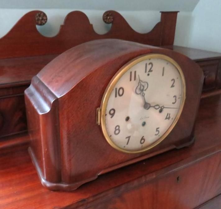 Wooden mantel clock with round face, set on a dark wood surface.